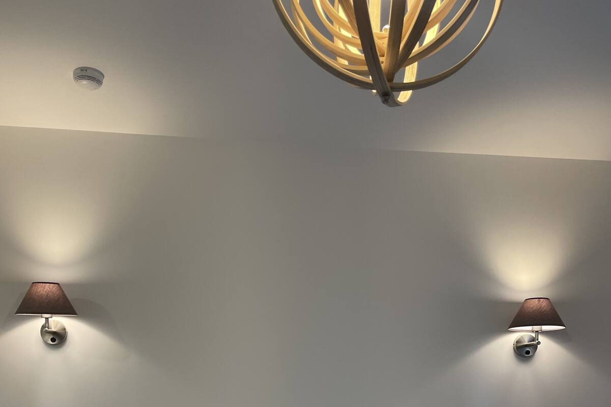 A neatly made bed with a wooden headboard, two wall-mounted lamps, and a ceiling light fixture.