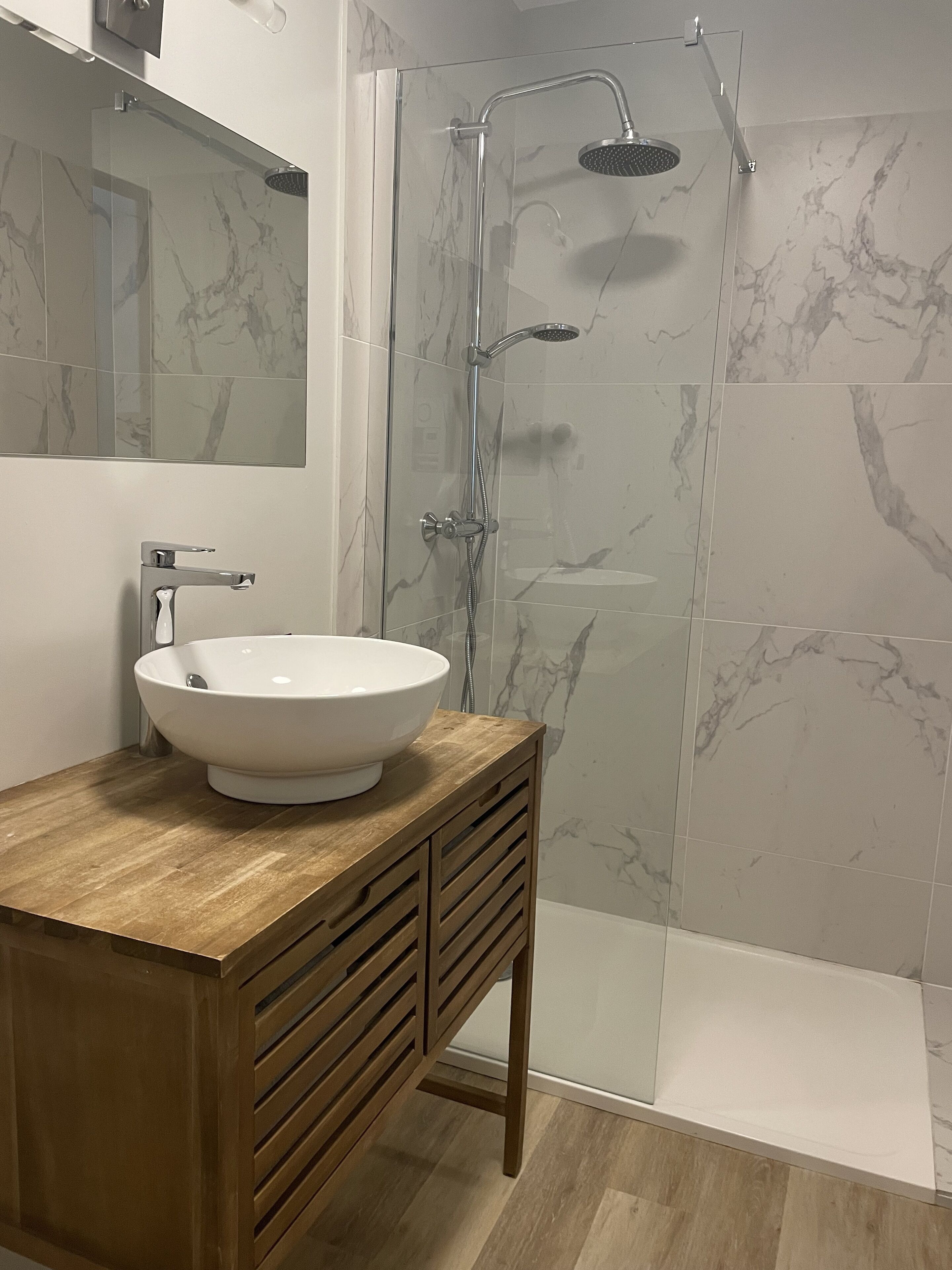 A bathroom with a wooden vanity, a white sink, and a glass shower enclosure.
