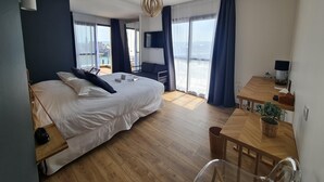 A modern hotel room with a large bed, a wooden desk, a chair, a TV, and a balcony with a view. - La Tour Aux Crabes (Dieppe)