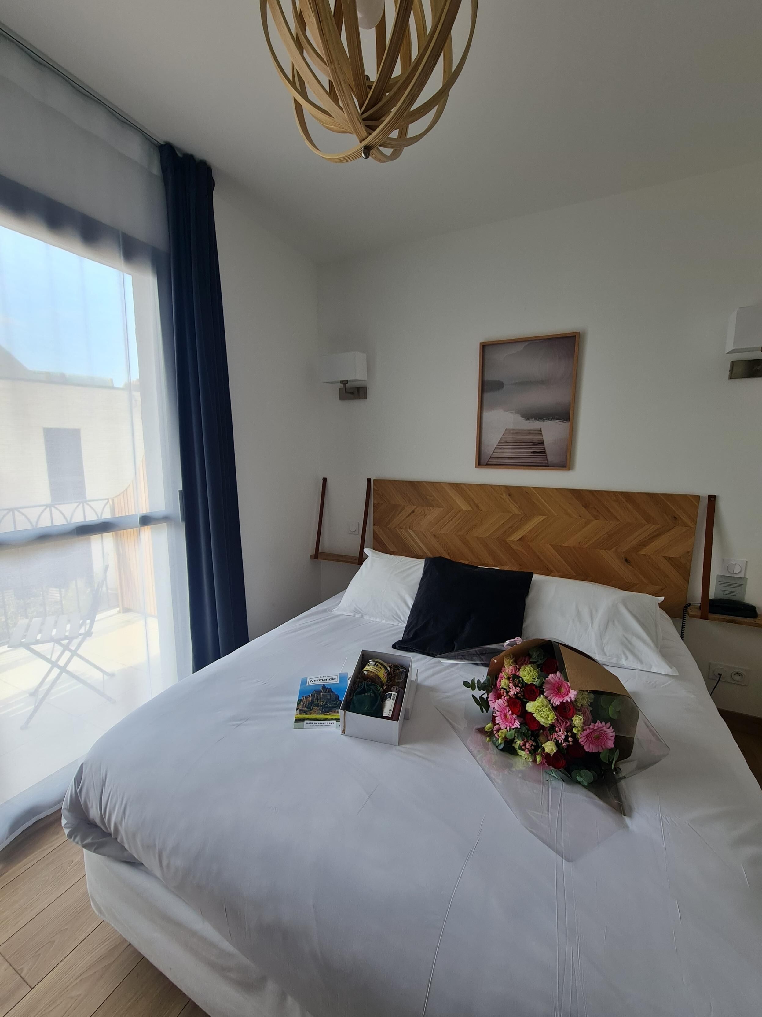 A hotel room with a large bed, a wooden headboard, a view of the outside balcony, and a framed picture on the wall.