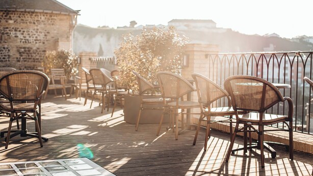 A wooden deck with wicker chairs and a table, overlooking a body of water and a stone building. - La Tour Aux Crabes (Dieppe)