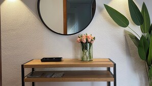 Una consola de madera con un espejo, un florero con flores y dos lámparas fijadas a la pared.