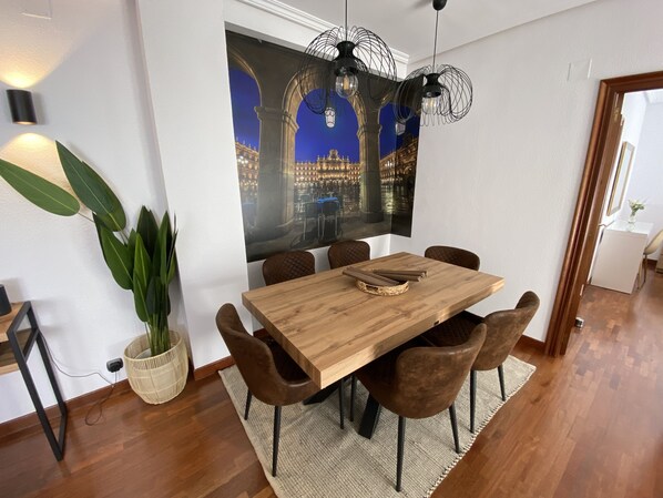 Ein Essbereich mit Holztisch, sechs Stühlen, einer großen Wanddekoration und einem Blumentopf.