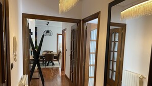 Un pasillo con suelo de madera, una zona de comedor con mesa y sillas, y un espejo grande que refleja la habitación.