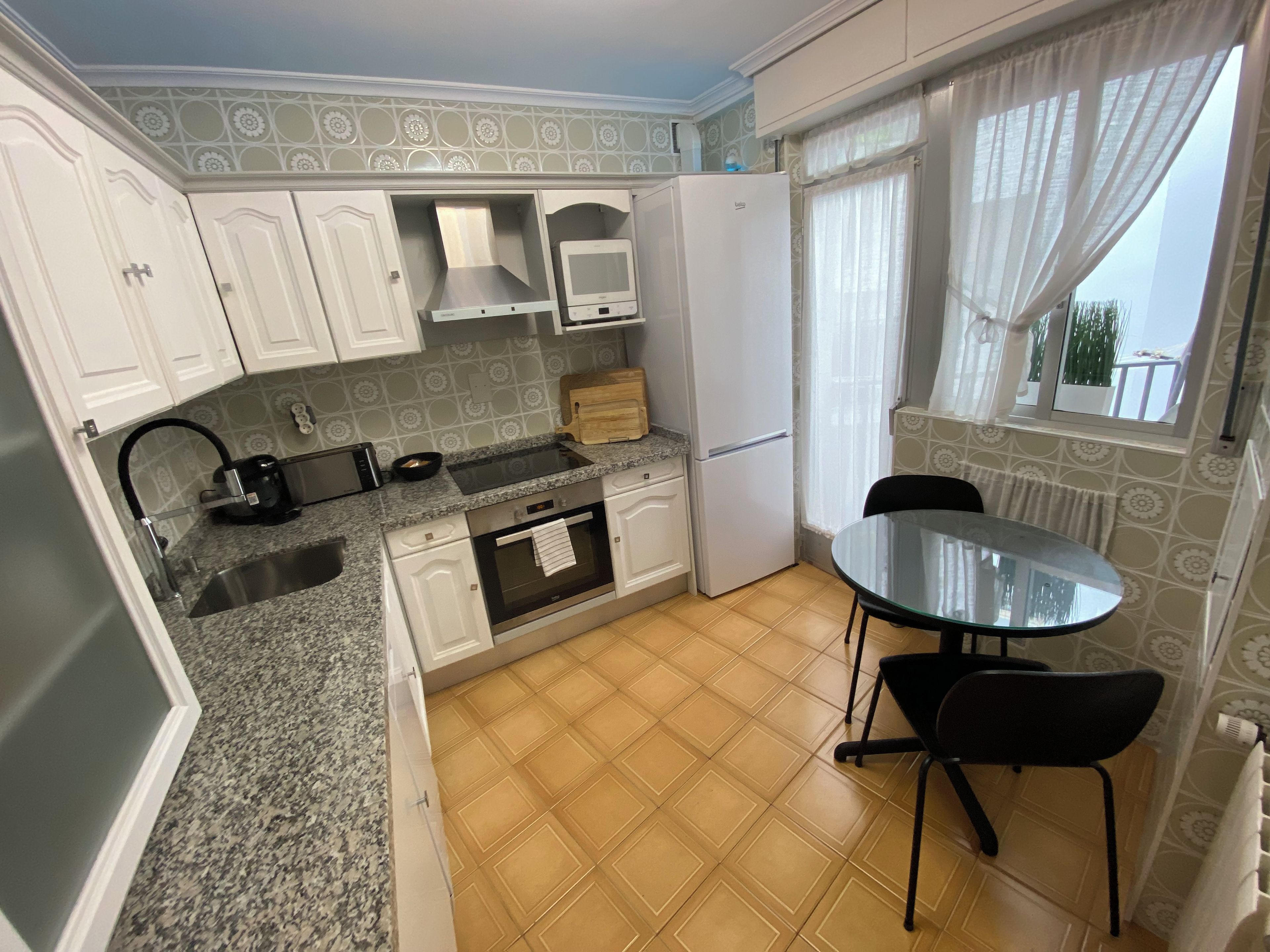 Cocina compacta con fregadero, estufa y un pequeño comedor con mesa y sillas.