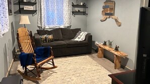 Ein Wohnzimmer mit einem dunkelgrauen Sofa, einem Holzschaukelstuhl, einem Deckenventilator und einem Holztisch.