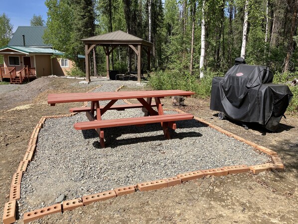 A picnic area with a wooden table and benches, surrounded by gravel and a brick border.