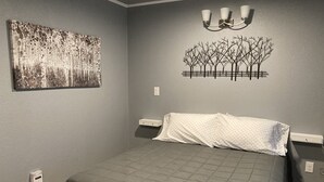 Ein Schlafzimmer mit einem Bett, einer Wandleuchte, einem Gemälde und einer Steckdose.
