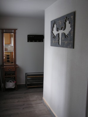 A room with a wooden cabinet, a mirror, a black shelf, and a wall-mounted artwork.