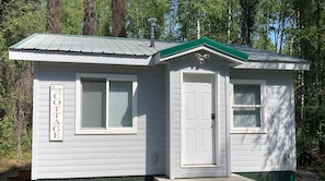 A small, single-story cottage with a green roof and white siding, labeled "Welcome to our COTTAGE."
