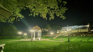 A gazebo with a dome roof in a well-lit garden at night.
