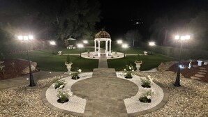 A well-lit garden with a gazebo, stone pathways, and neatly arranged flower beds.