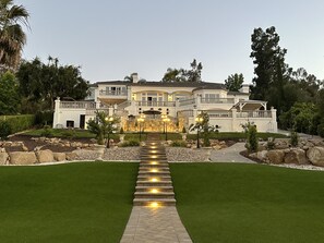 Una casa grande de varios pisos con un césped cuidado, un camino de piedra que conduce a la entrada e iluminación exterior.