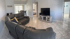 A modern living room with a leather sofa, a flat-screen TV on a white stand, and a dining area in the background. - Tampa home (Tampa)