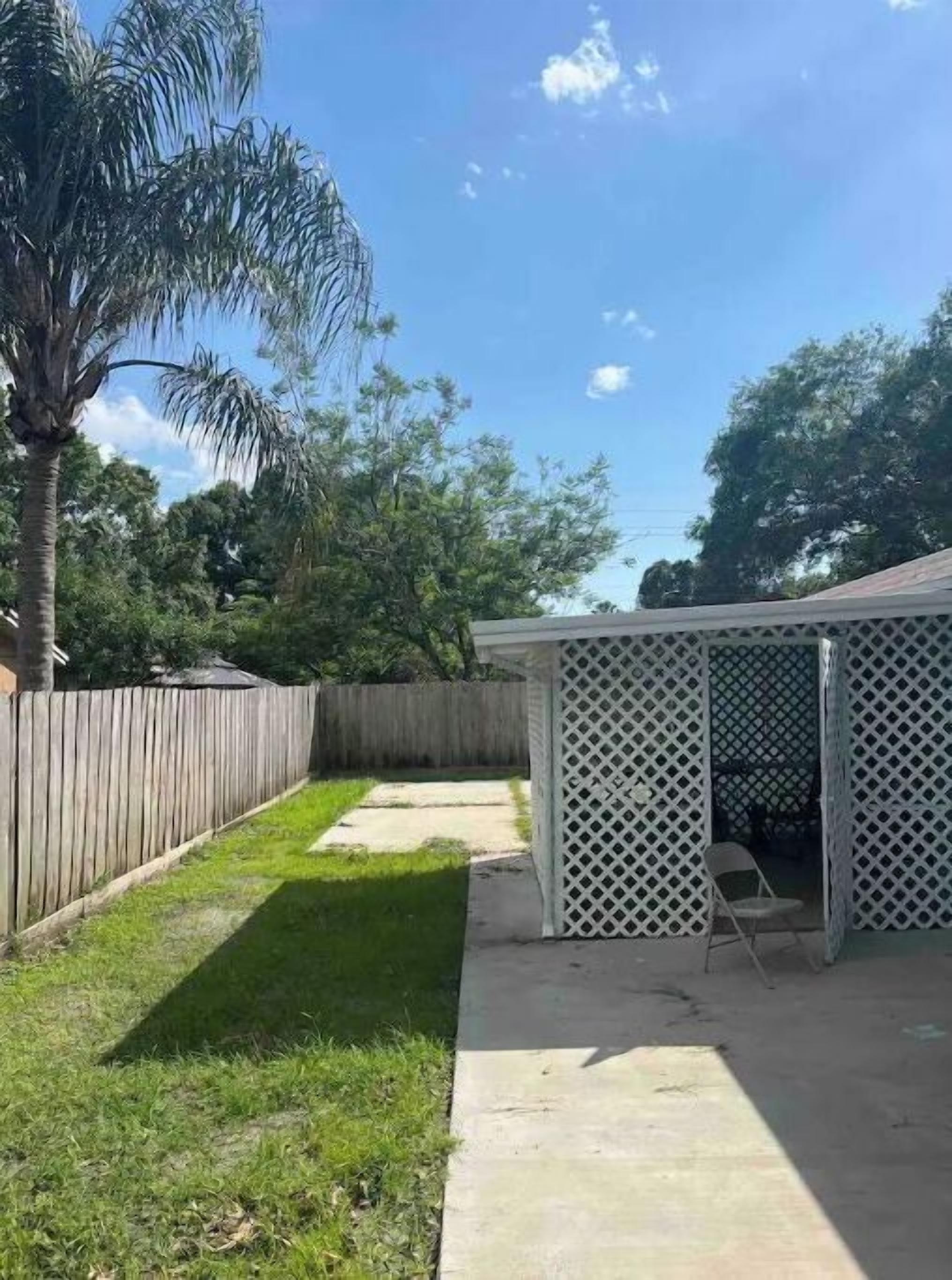 A backyard with a wooden fence, a palm tree, and a covered patio area.