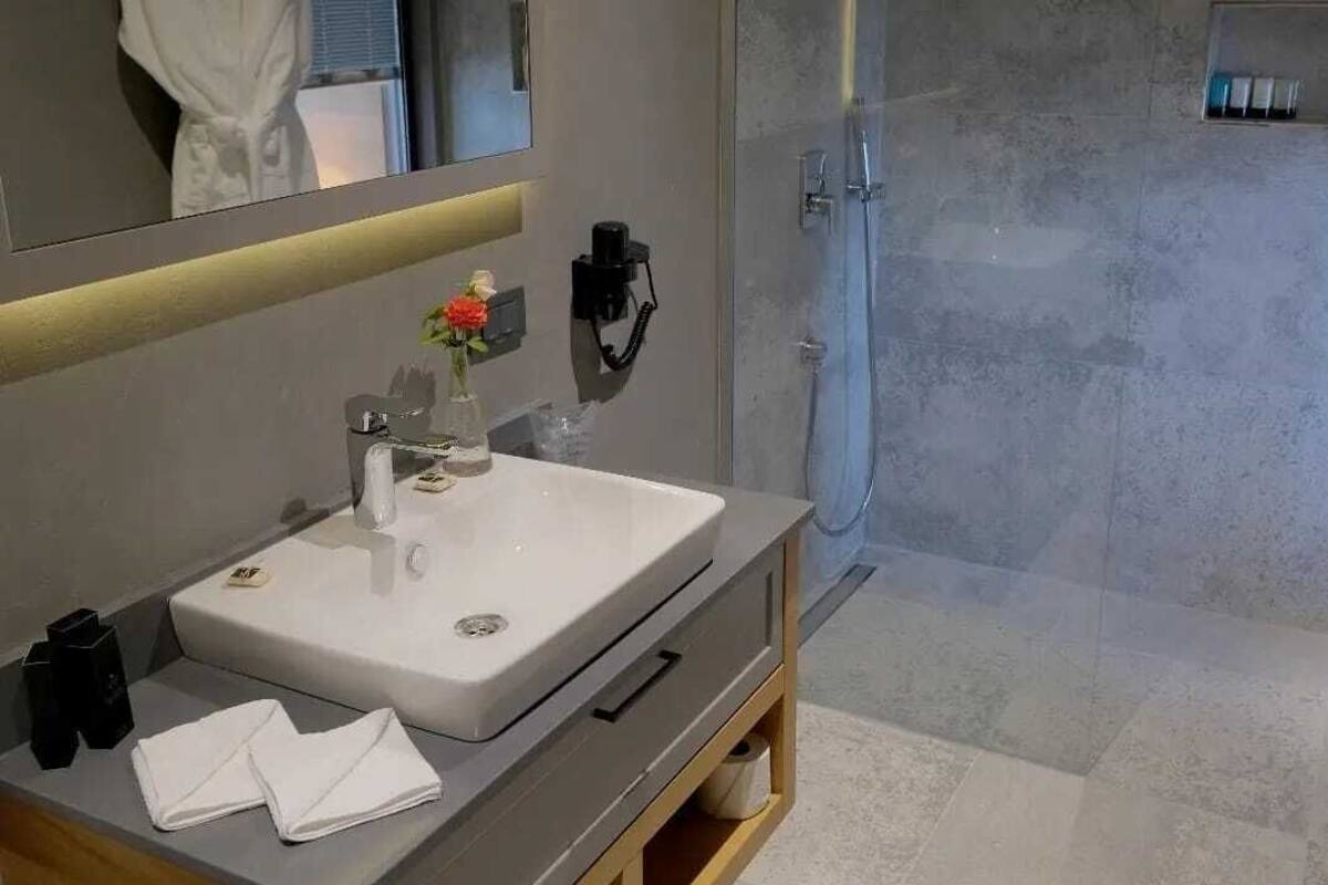 Uma casa de banho moderna com um espelho grande, uma pia branca, um chuveiro manual e um toucador de madeira.