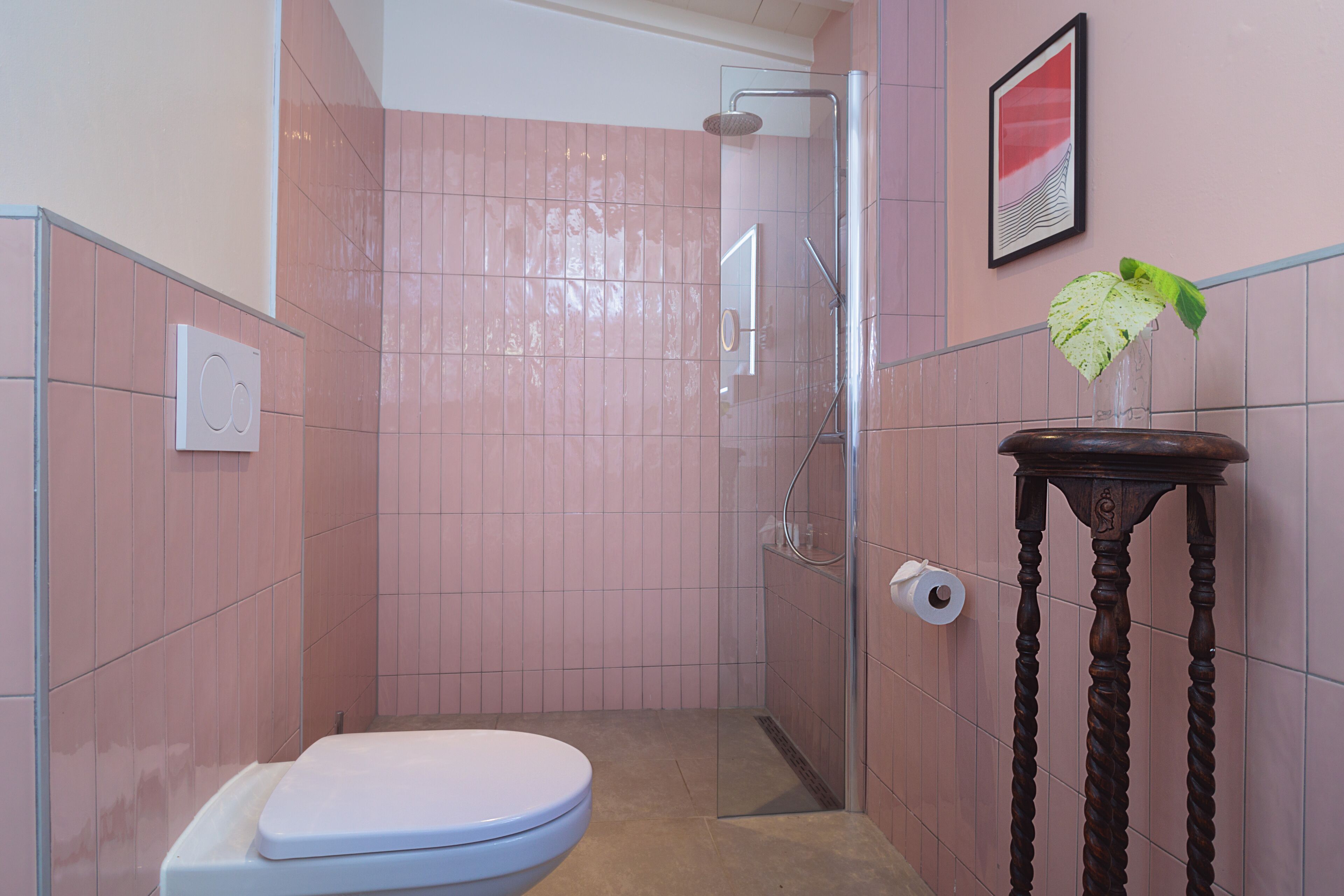 Un baño con ducha, inodoro y una mesita con una planta.