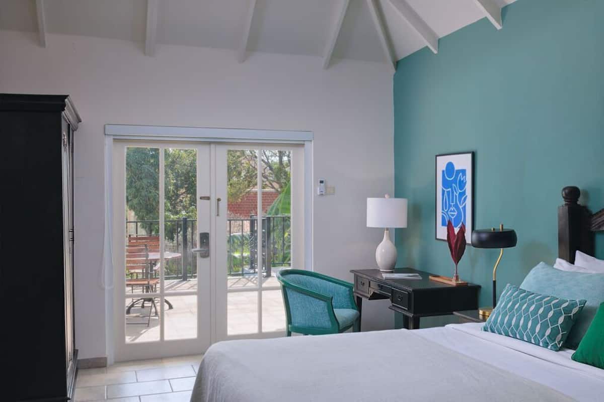A bedroom with a bed, a desk, a chair, a lamp, and a sliding glass door leading to an outdoor area.