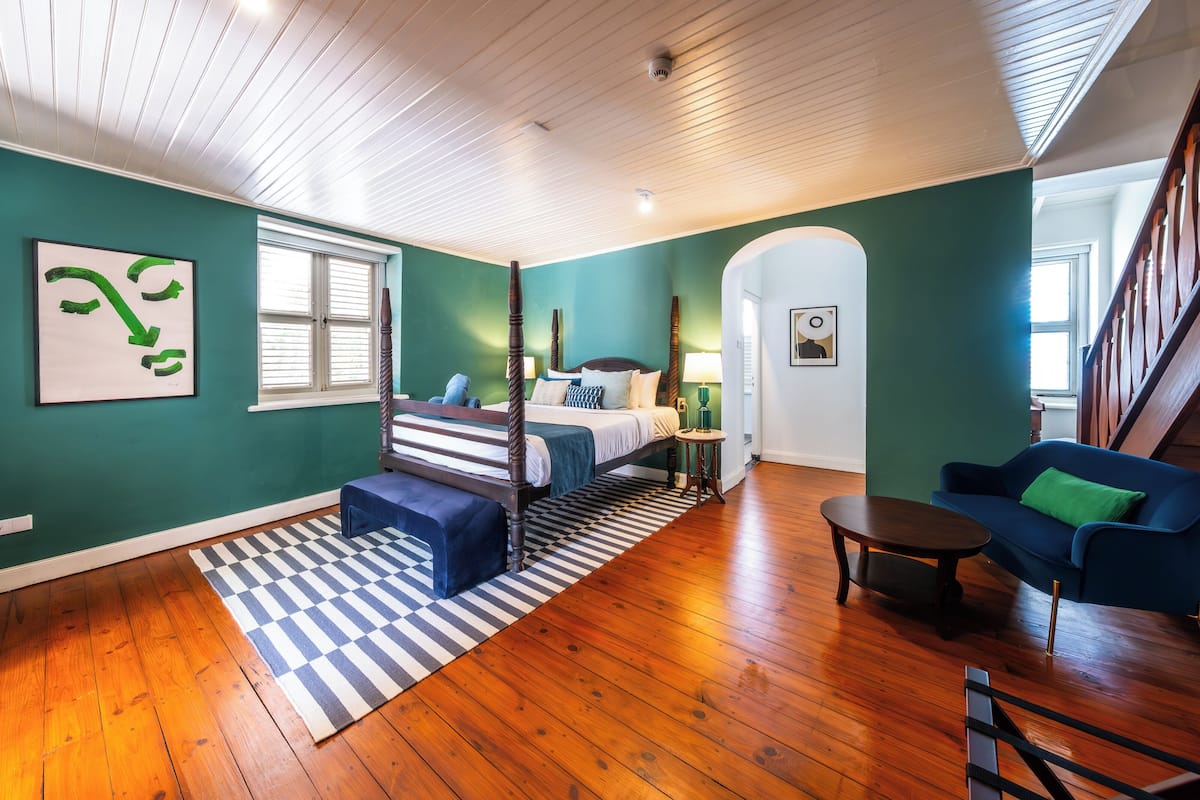 A room with a bed, a blue sofa, a wooden floor, and a checkered rug.