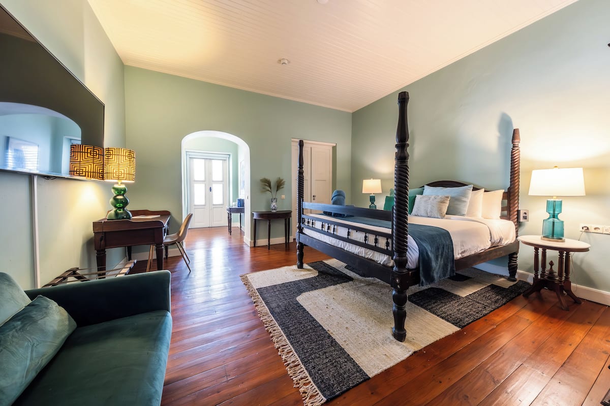 A bedroom with a four-poster bed, a desk, a chair, and a couch.