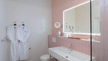 Un baño con un lavamanos blanco, un espejo y dos albornoces blancos colgados en la pared.