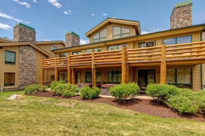 A two-story log cabin with a covered porch, stone chimneys, and a well-maintained lawn.
