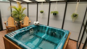 Uma banheira de hidromassagem com cadeiras de madeira e plantas em vasos em uma área externa coberta.