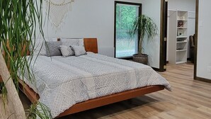 Quarto com cama, ventoinha no teto, janela ampla e planta em vaso.