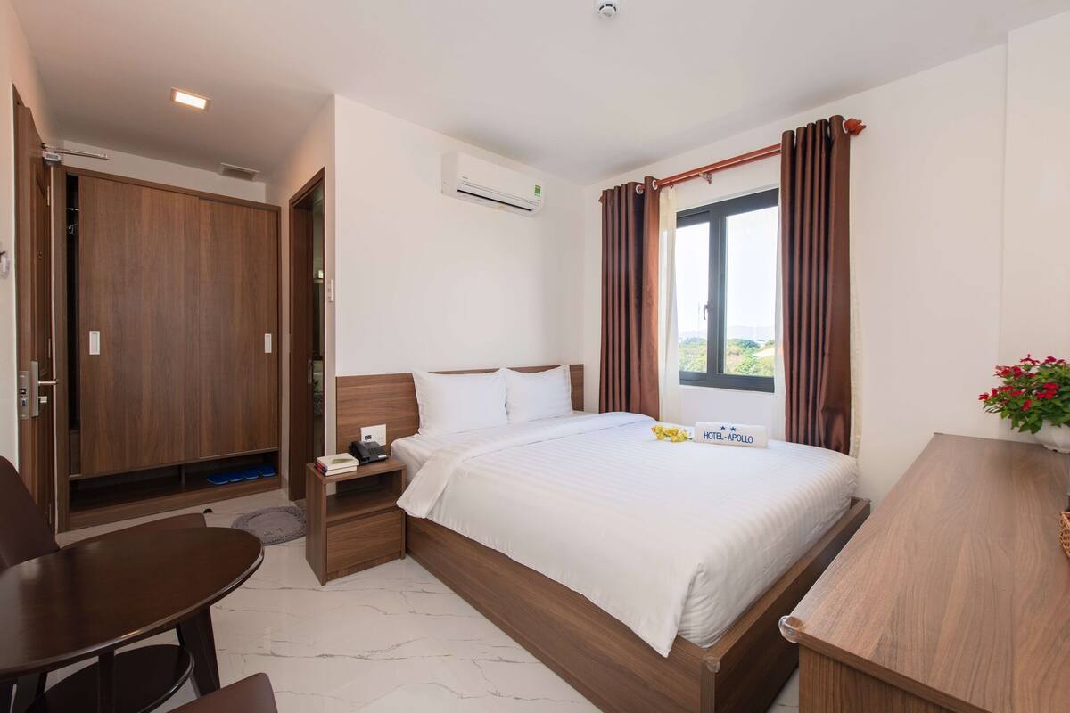 Quarto de hotel com cama, escrivaninha, cadeira, guarda-roupa e ar condicionado.