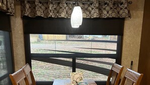 A dining area with a wooden table, four chairs, a decorative ceiling light, and a view through a large window. - Private Luxury Camping Experience  (Asheville)