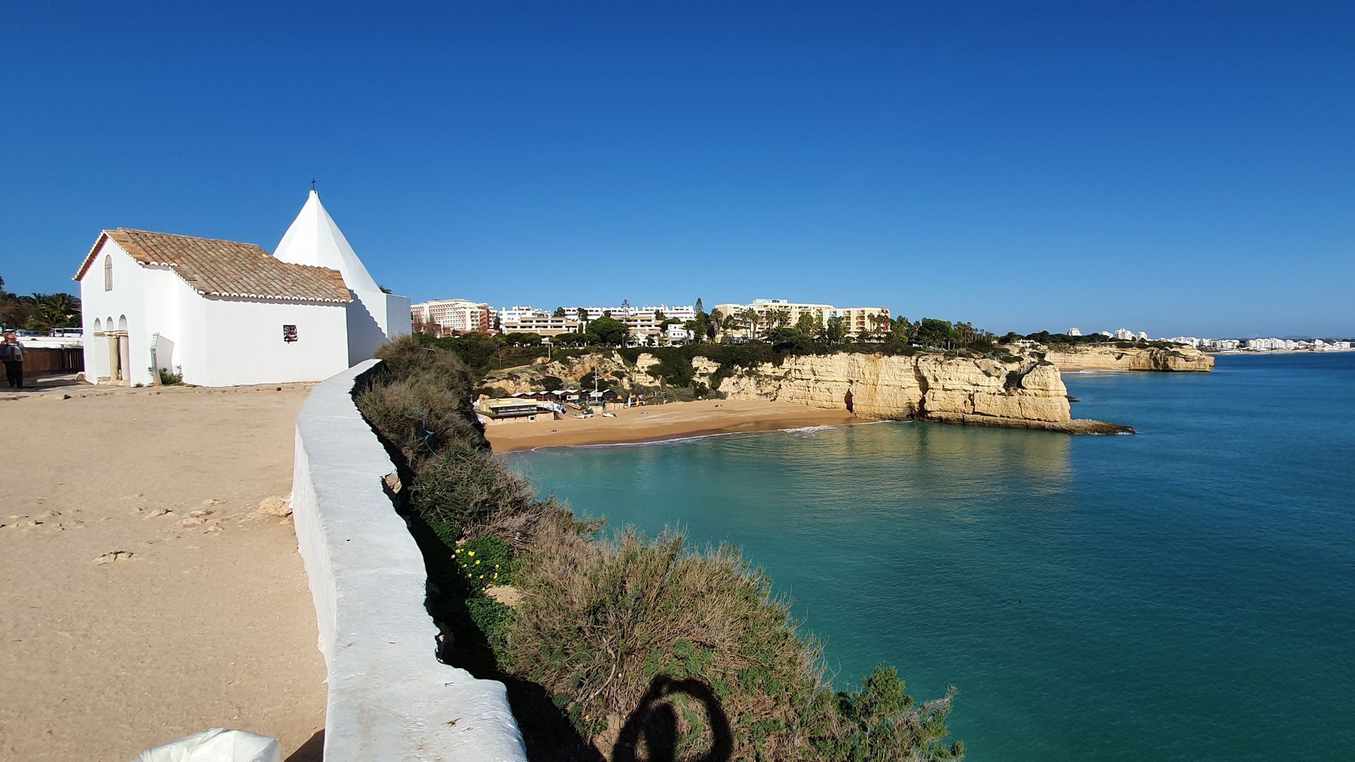 Eine Küstenlandschaft mit einem weißen Gebäude, einem Sandstrand und einer felsigen Küstenlinie.