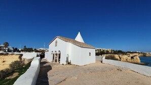 A small white church with a bell tower, located on a sandy beach with a clear blue sky. - The Algarvean Oasis with Pool by LovelyStay (Alporchinhos)