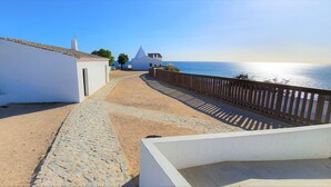 A coastal walkway with white buildings, a cobblestone path, and a wooden fence overlooking the sea. - The Algarvean Oasis with Pool by LovelyStay (Alporchinhos)