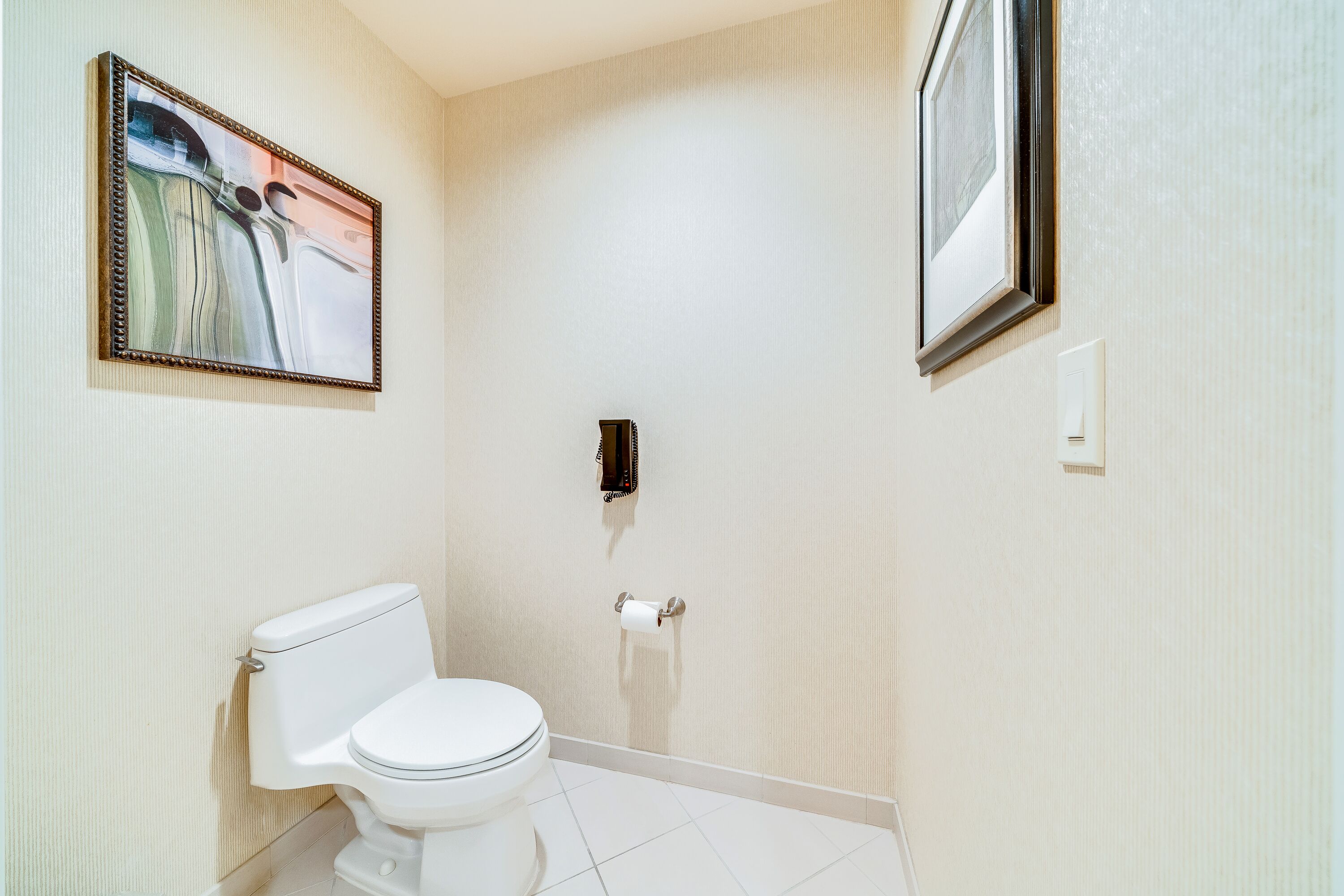 A bathroom with a toilet, a framed abstract painting, and a mirror on the wall.