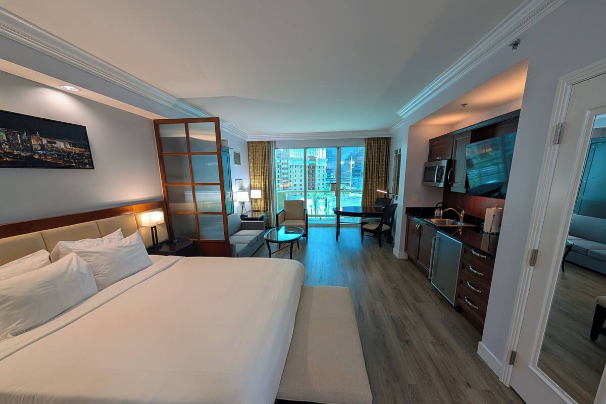 Een hotelkamer met een groot bed, een bureau, een stoel, een kleine tafel, een televisie en een kitchenette.