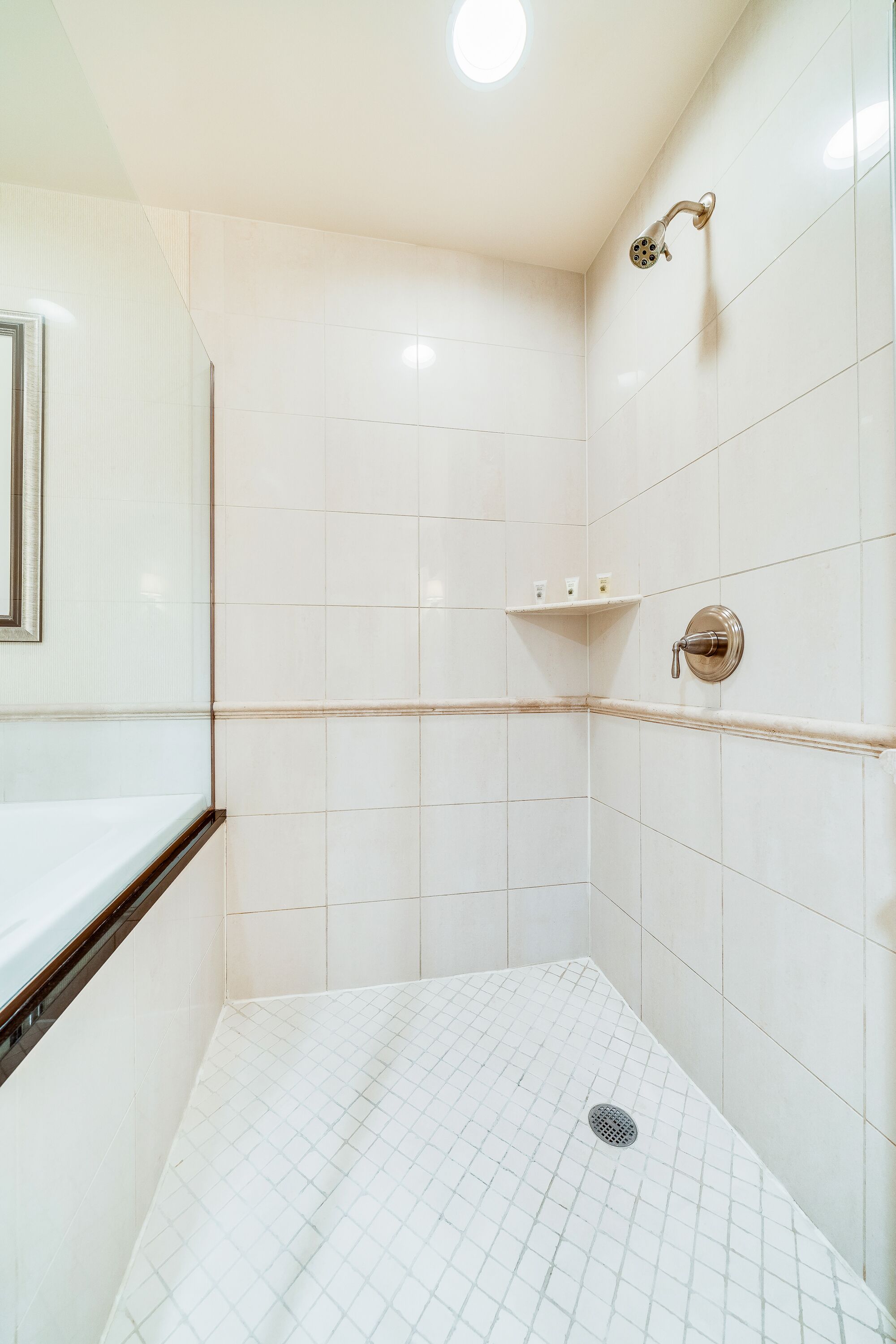 Ein modernes Badezimmer mit weißen Fliesen, einer Dusche inklusive Handbrause und einer kleinen Ablage für Toilettenartikel.