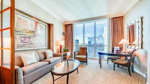 A spacious living room with a large window, a sofa, a coffee table, and a dining area. - Jet Luxury Elite at The Signature (Las Vegas)
