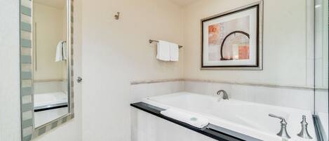 Un baño moderno con una bañera grande, un espejo y una obra de arte enmarcada en la pared.