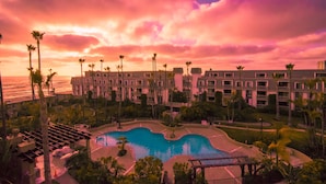 Ein Resort mit Pool, Palmen und Blick auf den Ozean bei Sonnenuntergang.