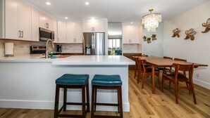 A modern kitchen with white cabinetry, stainless steel appliances, and a central island with bar stools.