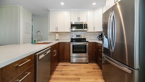 A compact kitchen with stainless steel appliances, wooden cabinets, and a white countertop.