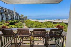 A balcony with three chairs, a view of the ocean, and a building with multiple balconies in the background.