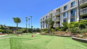 A well-maintained courtyard with a putting green, surrounded by multi-story buildings with balconies and a clear blue sky.