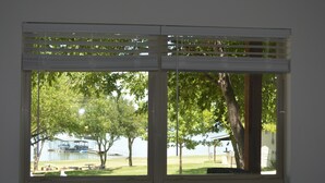 A room with a large window overlooking a grassy area with trees and a dock.