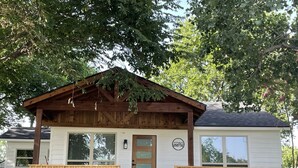 A wooden cabin with a front porch, a mailbox, and a number sign.