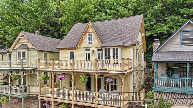 A multi-story house with a balcony, a stone foundation, and hanging flower baskets. - Downtown House w/Parking! On Spring St, Hot Tub! (Eureka Springs)