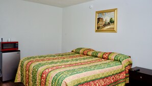 Een kamer met een bed, een kleine koelkast en een schilderij aan de muur.