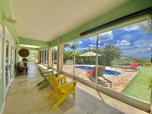 A spacious indoor area with a view of a swimming pool and greenery outside.