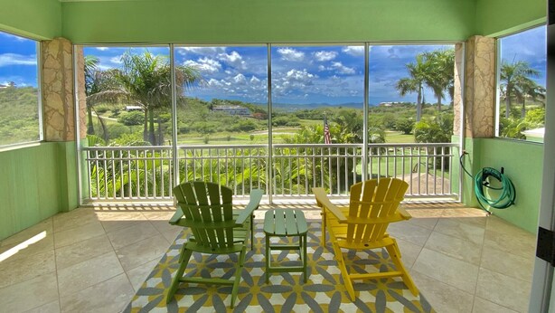 Een balkon met twee groene en één gele Adirondack-stoel, een klein tafeltje en een decoratief vloerkleed.