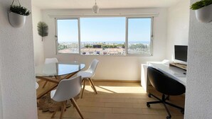 Un espace de vie moderne comprenant un coin repas, un espace de travail et une grande fenêtre donnant sur la ville.